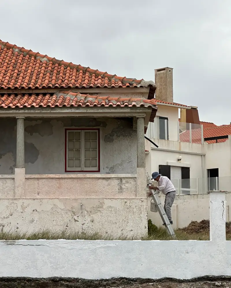 Ouvrier sur une échelle rénovant la façade d’une maison